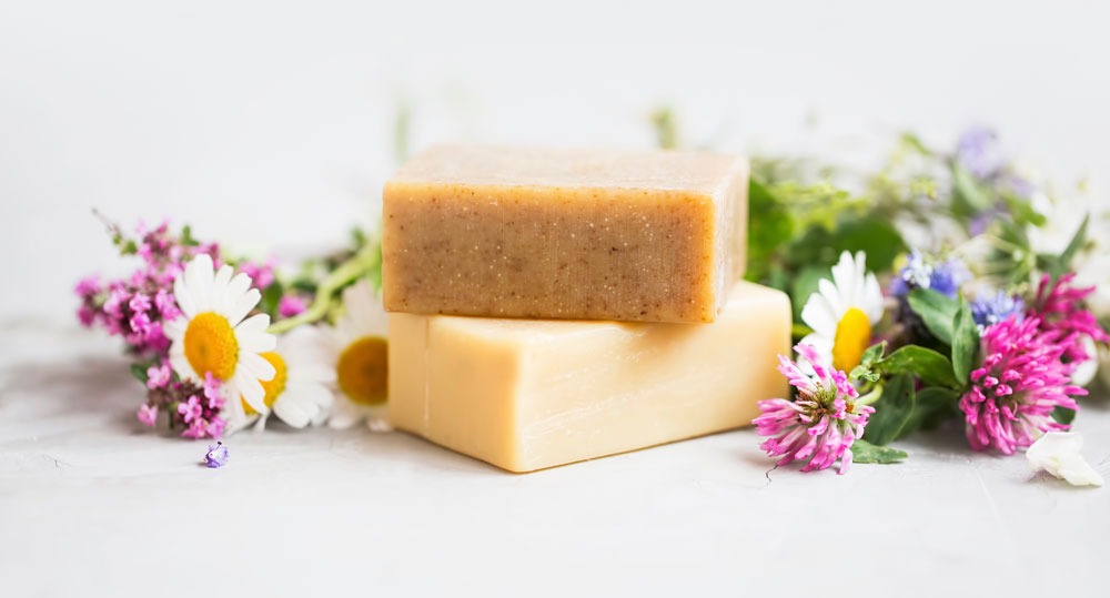 Handmade soap bars with chamomile and clover flowers on white background